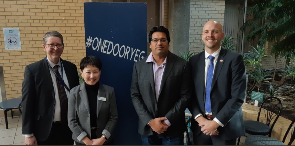 Mr. Rohit Gupta with 3 other people with #OneDoorYeg poster behind.